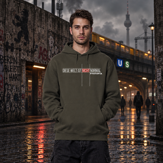 Düstere Berliner Street Scence. Im Hintergrund der Fernsehturm und eine S-Bahn Brücke. Darunter einige dunkle bekleidete Menschen. Im Vordergrund ein junger Mann. Er trägt einen dunkelgrünen Hoodie mit dem Print "Diese Welt ist nicht normal. Vystopia".