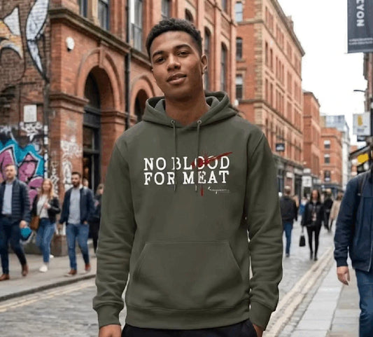 Junger Mann trägt einen olivgrünen Hoodie mit dem Aufdruck 'NO BLOOD FOR MEAT' in einer belebten Einkaufsstraße mit alten Gebäuden aus roten Klinkern– vegane Statement Mode.